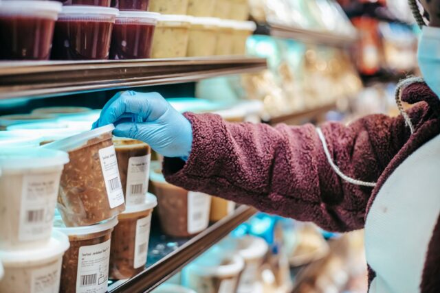 Mână care ține un produs alimentar într-un magazin, cu eticheta nutrițională întoarsă spre cumpărător