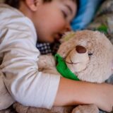 Copil care își ține ursulețul de pluș în brațe în sala de așteptare a unui cabinet de pediatrie