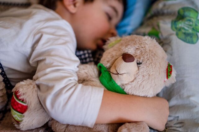 Copil care își ține ursulețul de pluș în brațe în sala de așteptare a unui cabinet de pediatrie