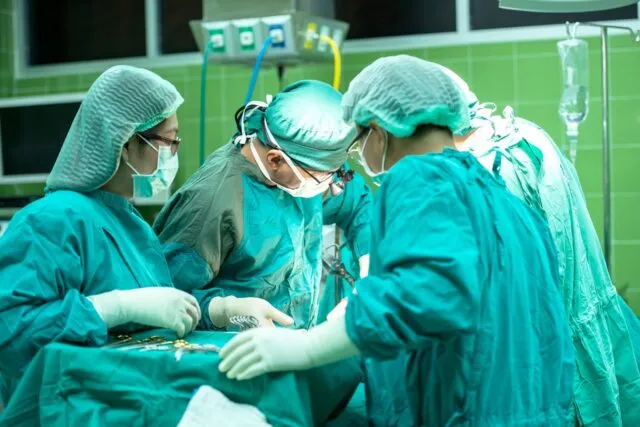 Medic care ascultă un pacient, cu un telefon și un carnet pe birou între ei